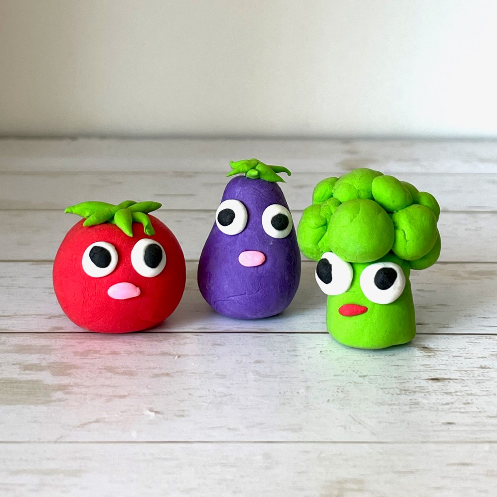 Three funny clay vegetables figurines - a funny broccoli, tomato and eggplant with big eyes