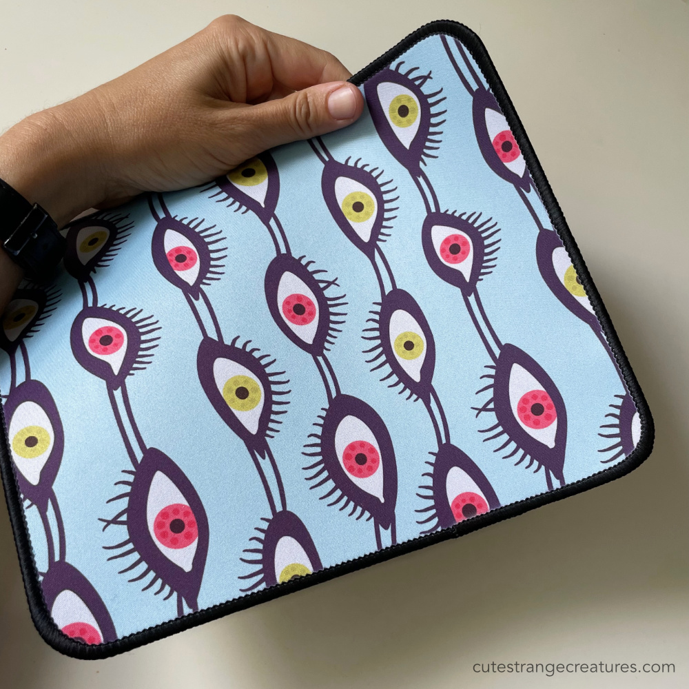 psychedelic mousepad with bright green and pink eyes over light blue background held in hand