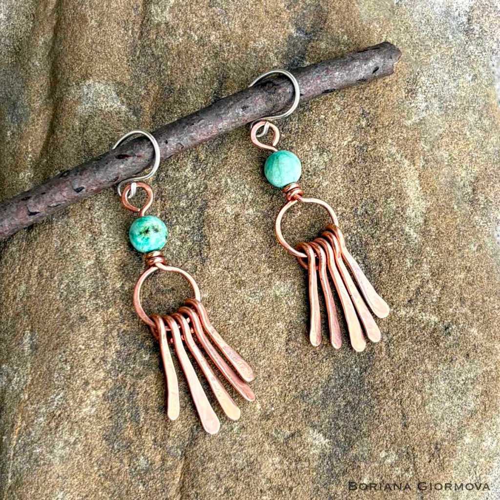 copper dangle earrings with turquoise gemstones and teardrop shaped elements shot on a stone hanging from a tree branch