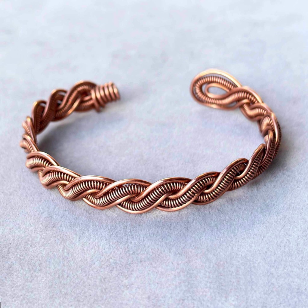 Ръчно плетена отворена регулируема медна гривна от рециклирана мед снимана на неутрален фон