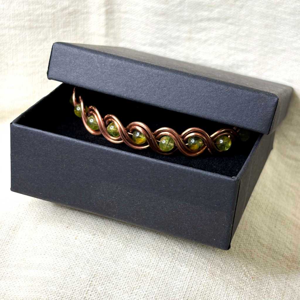 handmade copper cuff bracelet - wire woven with 5 mm peridot gemstones in a black jewelry box with half open lid