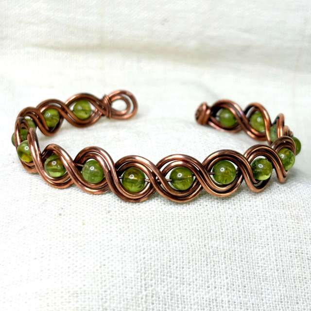 handmade copper cuff bracelet - wire woven with 5 mm peridot gemstones, shot on soft white fabric