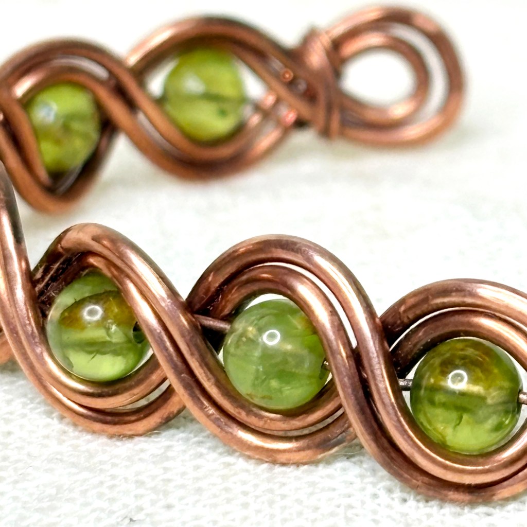 close up on wire wrapped copper bracelet with 
peridot sotnes