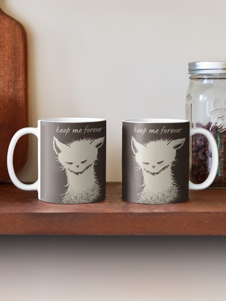 Two ceramic mugs featuring a cream-colored sleeping cat illustration and the words “keep me forever,” displayed on a wooden shelf beside a glass jar
