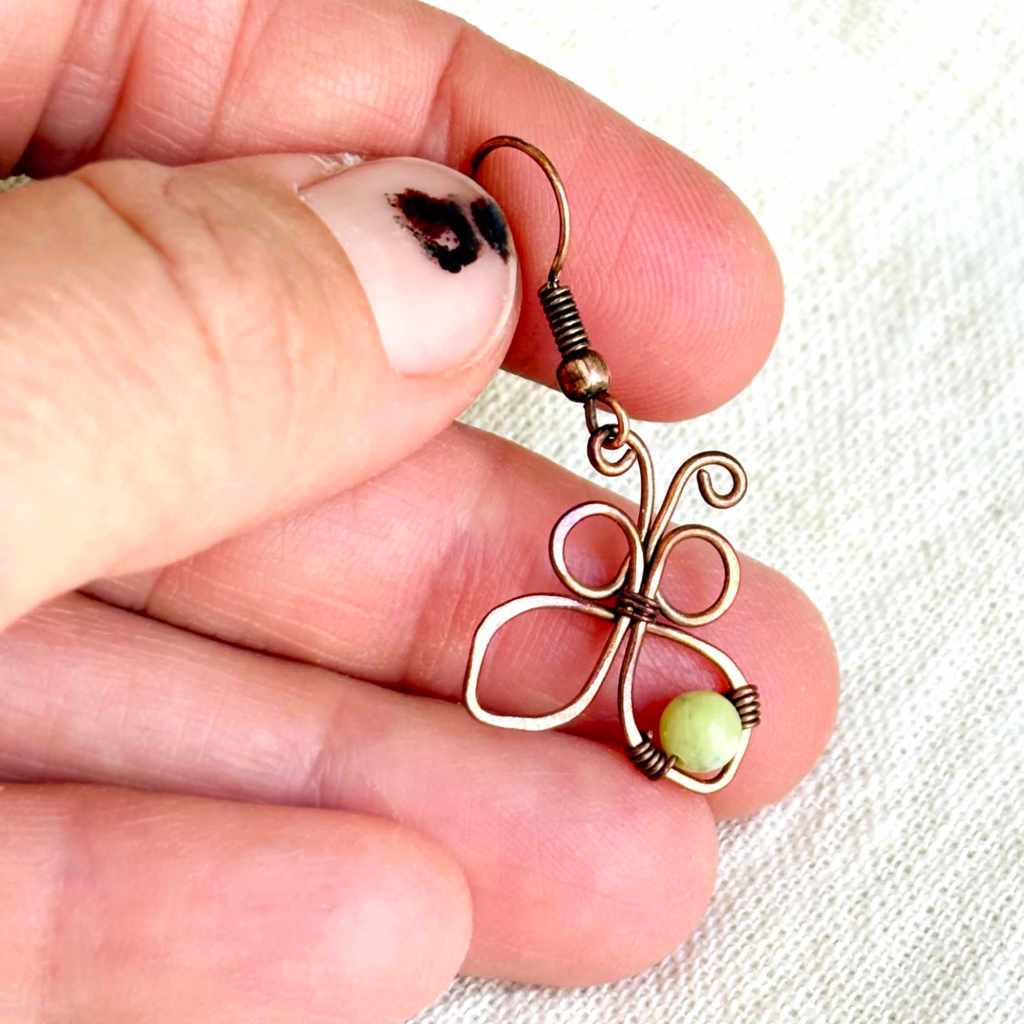 Handmade copper butterfly earring held between fingers, showing its small size and wire wrapped details