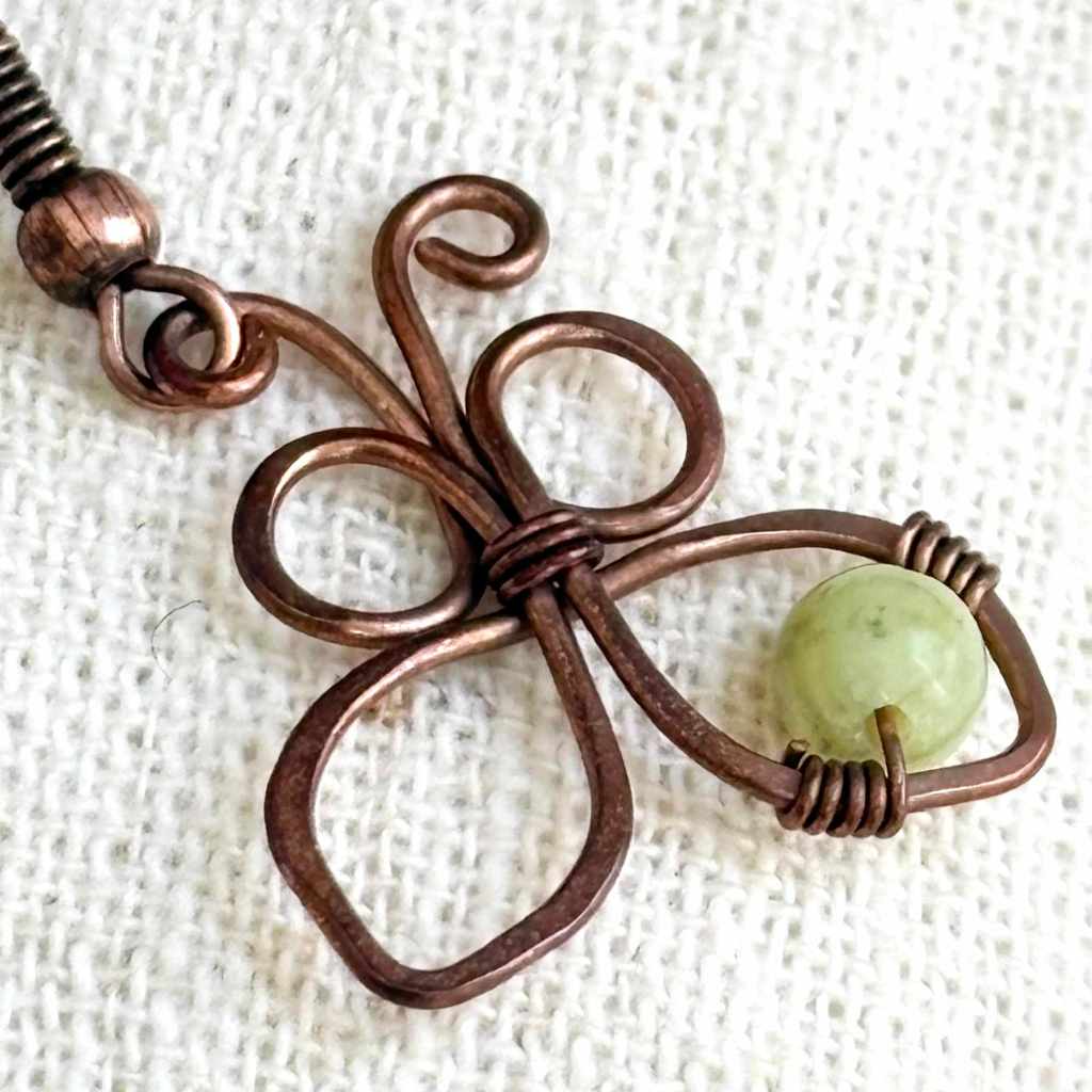 Close-up of a handmade copper butterfly earring showing wire wrapping, copper texture and natural green stone