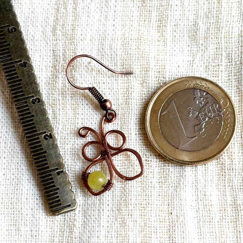 Handmade copper butterfly earring beside a ruler and euro coin showing its approximate size